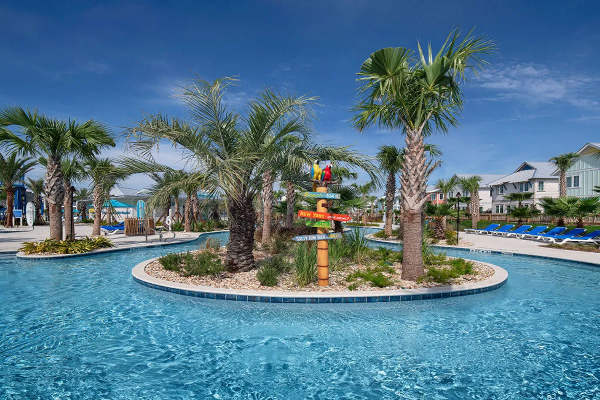 The scene captures a picturesque lazy river winding through a tropical landscape dotted with palm trees and blue lounge chairs. A playful, colorful signpost with parrots adds a fun, vacation vibe. Families and children are seen floating and swimming in the lazy river and playing near a waterslide area, while others relax on sun-drenched loungers.