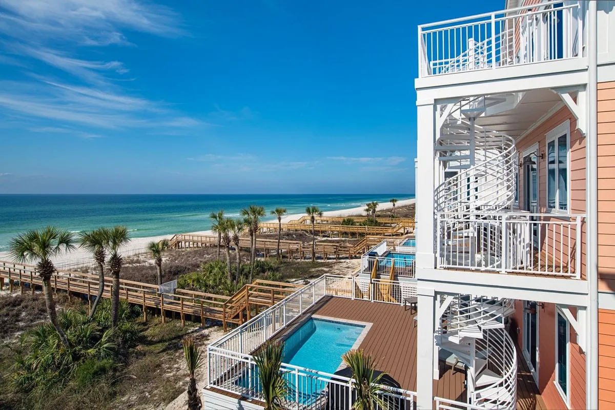 This image features a private heated pool adjacent to a beachfront villa, with a spiral staircase and direct wooden dune walkover paths leading to the sand. The pool area is framed by ocean views and a luxurious outdoor lounging setup, capturing the seamless connection between poolside relaxation and direct beach access.